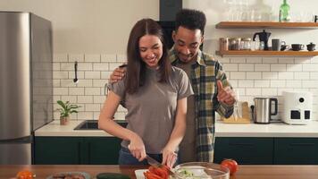 Multicultural couple enjoying a joyful morning in the kitchen as the camera moves from wide shot to close-up - woman slices salad while man dances nearby video