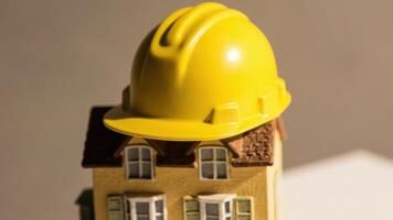 A small model house with a yellow construction hard hat sits on a flat surface. photo