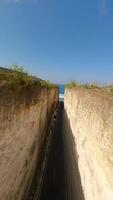 Immersive FPV drone flight along coastal road carved between limestone cliffs and turquoise waters at Batu Barak Beach, Bali, Indonesia. video