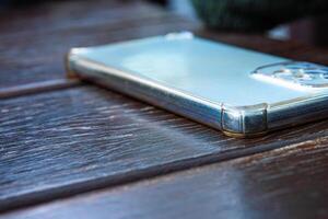 Closeup of the smartphone with silver body and a transparent protective case placed on a dark wooden table. Selective focus photo