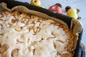 Homemade apple cake with a golden crust in a baking tray, placed on a rustic white wooden table with fresh apples and walnuts 05 photo
