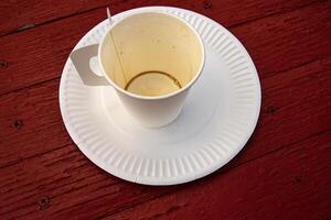A white paper coffee cup with a handle placed on a white paper plate set on a rustic red wooden table in an outdoor cafe in Hamina, Finland 06 photo