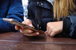 Woman using a smartphone, actively scrolling on a touchscreen, while sitting at an outdoor cafe wooden table. Selective focus 10 photo
