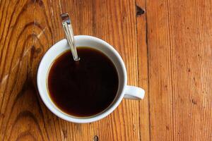 Minimalist top view of a white coffee cup with etal spoon placed on a textured wooden table or windowsill surface. 13 photo