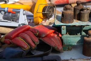 Tervasaari, Hamina, Finland, August 26th, 2023. Closeup of red leather work gloves with Finstar Union label, and antique weights arranged on a metal table at a Finnish coastal flea market photo