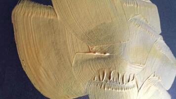 Brushing broad strokes of metallic gold paint on canvas. dynamic movement and texture. video