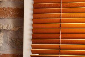 Closeup of a partially open wooden venetian blind next to a rustic textured wall made of brick and plaster. Selective focus 05 photo