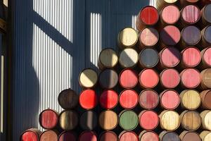 Colorful Stacked Wine Barrels in a Sunlit Warehouse Creating Unique Shadow Patterns on a Rustic Metal Wall photo