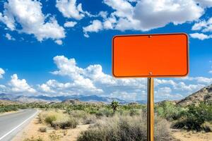 Blank Orange Sign on Desert Road with Dramatic Sky and Scenic Mountains in the Background Under Bright Sunlight photo