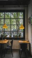 Cozy cafe interior with simple and stylish design features yellow pendant lights, wooden tables, and potted plants by large window, creating warm and inviting atmosphere photo