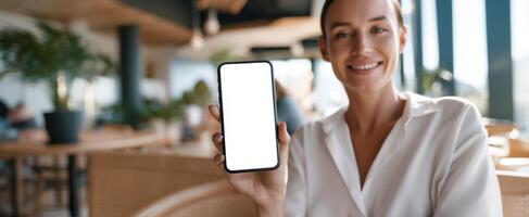 The smiling woman showcasing a smartphone in a modern cafe setting. photo