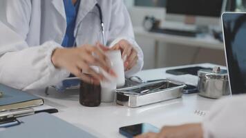 A doctor is working on a laptop while a patient sits at a desk video