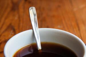 A closeup of a white ceramic cup filled with black coffee, with a metal spoon inside, placed on a rustic wooden table.Soft focus 09 photo