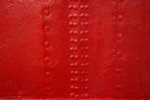 A closeup view of an industrial red painted metal surface with symmetrical rows of rivets, reflecting shipbuilding or machinery design textures 19 photo