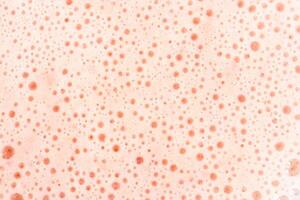 Foam texture with small bubbles on a light pink background. Close up macro view of liquid surface with air bubbles. Smooth beverage background. photo