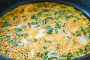Green onion omelet in frying pan, a breakfast food idea. Macro shot of fresh eggs and herbs prepared for healthy meal concept. photo