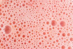 foam texture with small bubbles on a light pink background. Close up macro view of liquid surface with air bubbles. Smooth beverage background abstract concept. photo