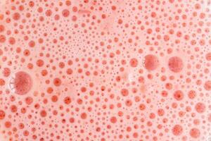 Pink foam texture with small bubbles on a light pink background. Close up macro view of liquid surface with air bubbles. Smooth beverage background abstract concept. photo