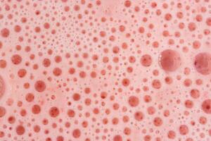 Macro shoot of pink foam texture with small bubbles on a light pink background. Close up macro view of liquid surface with air bubbles. Smooth beverage background abstract concept. photo
