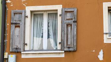 Weathered wooden shutters frame a charming window on a rustic building in a quaint village bathed in warm afternoon light photo