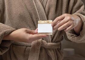 Closeup of woman in brown bathrobe with soap with blank label in hands, mockup photo