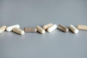 Mix of beige and brown medical capsules in a line on grey closeup. Dietary supplements and vitamins photo
