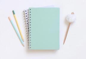 Blank spiral notebook on a white table near fur pen and pensils, school mockup photo
