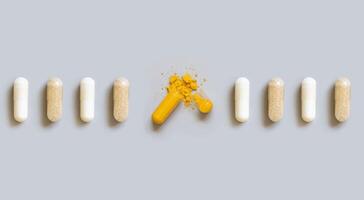 Beige medical capsules in a line with opened yellow one in the middle on grey top view photo