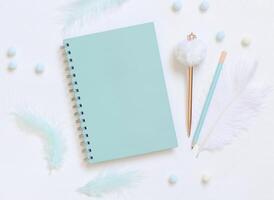 Blank spiral notebook on a white table near pastel feathers, pensil and fur pen, school mockup photo