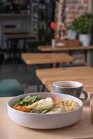 Bowl of couscous, meat, eggs and avocado and vegetables and cup of coffee on cafe table photo