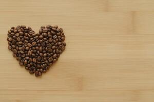 Flat lay photo of freshly roasted coffee beans forming heart on natural wooden rustic table with copy space. image for use in cafe menus or websites dedicated to coffee culture and love