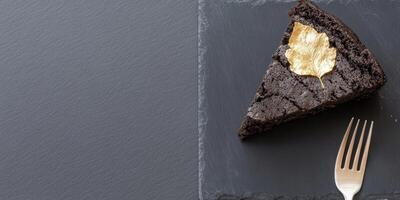 Elegant minimalist chocolate cake slice with gold leaf decoration on slate background photo