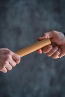 Teamwork driven by motivation and coordination. Two hands exchanging a wooden stick against a textured background. photo