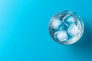 Glass of ice cubes on a vibrant blue background. Pure water unpolluted concept. photo