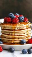 Stack of pancakes topped with berries and syrup on a plate. photo