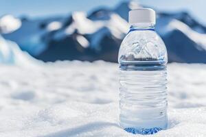 Clear water bottle on snow with mountains in the background. photo