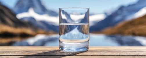 Clear glass of water with mountains and lake in the background. photo