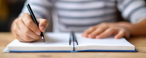 Person writing in a notebook with a pen on a wooden table. photo