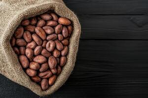 Brown cocoa beans spilling from a burlap sack on a dark wooden surface. photo