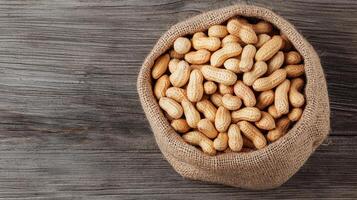 Burlap sack filled with peanuts on a wooden surface. photo