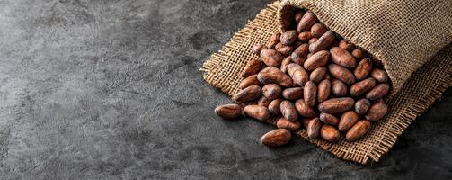 Cocoa beans spilling from a burlap sack on a textured surface. photo