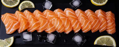 Fresh salmon sashimi garnished with lemon and ice on a dark platter. photo