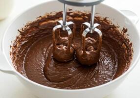 A close-up view of a mixer blending chocolate cake batter in a white bowl. photo