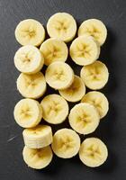 Overhead shot of neatly arranged, circular banana slices on a dark textured surface. photo
