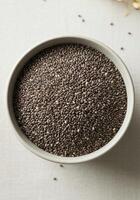 A full bowl of chia seeds viewed from above on a soft, white surface. photo