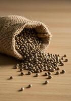 A burlap sack spills out a generous pile of hemp seeds on a wooden surface. photo