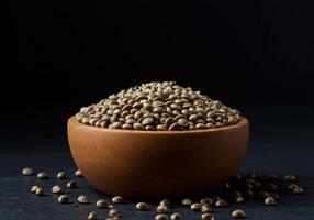 A wooden bowl filled with hemp seeds is placed on a dark, textured surface. photo