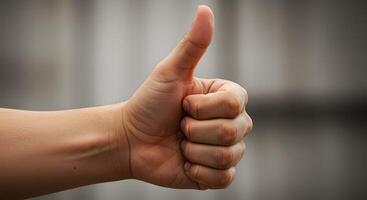 Hand giving a thumbs up gesture indicating approval or positivity in a soft-focused background photo