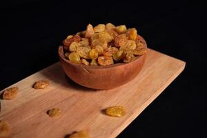 High angle view of a bowl of raisins on a wooden cutting board with a dark background. Food photography of a bunch of dried grapes commonly used in cooking and baking. photo