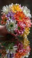 Colorful bouquet of flowers reflected in water with hand holding it during bright daylight photo